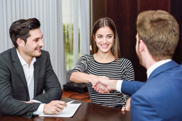 Smiling young couple shaking hands with an insurance agent or investment adviser